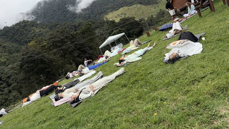 Participantes recostadas sobre mantas en una ladera verde, con montañas y neblina al fondo, en el Valle del Cocora